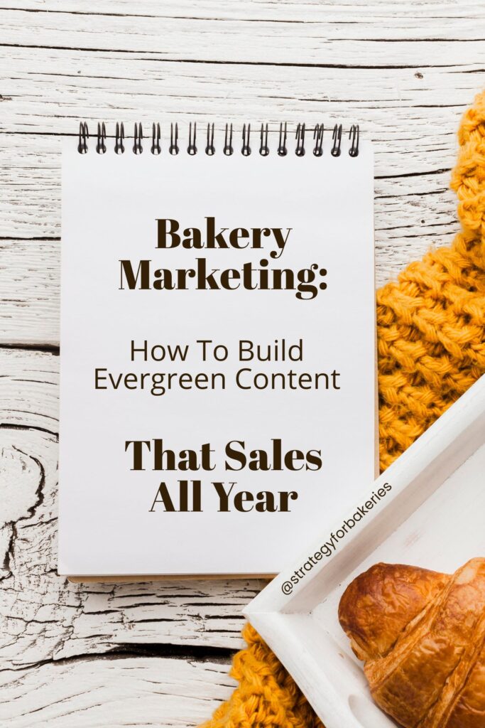 Spiral notebook on wooden table with text Bakery Marketing How To Build Evergreen Content That Sales All Year, next to a croissant and yellow knit fabric.