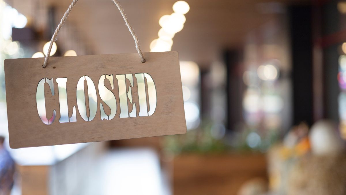 Close-up of a wooden sign with the word "CLOSED" cut out, hanging by a rope inside a blurred coffee shop interior.