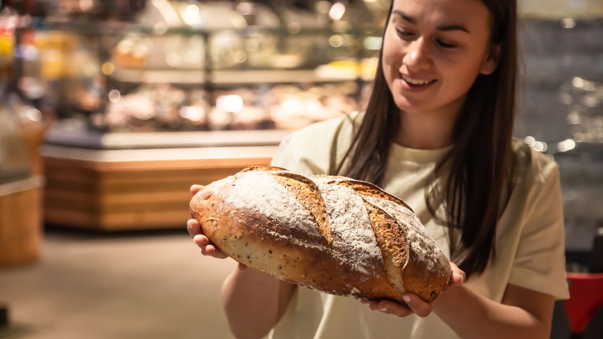 Smiling woman holding a rustic loaf of bread in a bakery, a moment from the routines behind bakery customer loyalty.